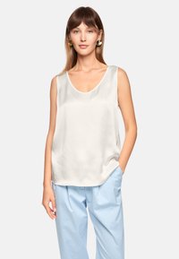 White satin tank top with a scoop neckline, featuring a loose fit. Paired with light blue trousers, showcasing a smooth texture.