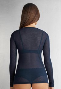Granatowa bluzka z długim rękawem w prążki o dopasowanym kroju, przezroczystym materiale i okrągłym dekolcie. Widok z tyłu ukazuje gładką sylwetkę.