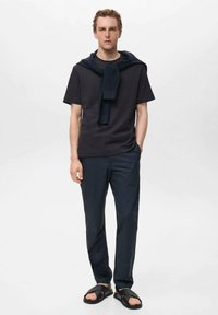 Cămașă scurtă de culoare bleumarin închis, pulover bleumarin pus pe umeri, pantaloni închiși la culoare și sandale negre de tip slide. Design simplu, aspect casual.