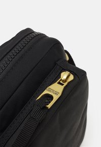 Sort stofpose med en guldfarvet lynlås med indgraveringen "Versace Jeans Couture" set på tæt hold.