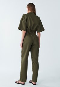 Monosuit verde oliva con mangas cortas, cintura elástica y corte recto. Tela suave y diseño minimalista.