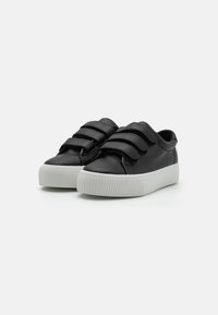 Black leather sneakers with three Velcro straps, featuring a white rubber sole and textured horizontal grooves. Round toe design.
