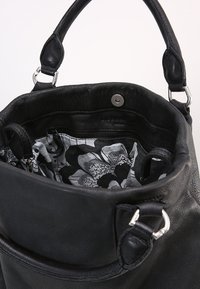 Czarna skórzana torebka z srebrnymi detalami, otwarte z góry, pokazująca czarno-białą podszewkę w kwiaty oraz wewnętrzną kieszeń na zamek.
