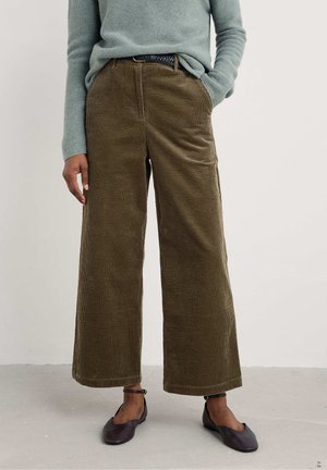 Wijdvallende corduroy broek in olijfgroen met een gestructureerde oppervlakte. Heeft een hoge taille en voorzakken. Gepaard met bruine flats.