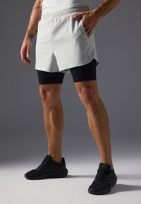 Γκρι αθλητικές βερμούδες με ελαστική ζώνη, πλάγιες τσέπες, επάνω σε μαύρες εφαρμοστές βερμούδες. Φοριούνται με μαύρα αθλητικά παπούτσια.