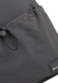 Sac en tissu gris avec une surface texturée, doté d'une fermeture à cordon et d'une étiquette de marque visible sur le côté.