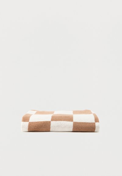 Serviette pliée avec un grand motif à damier beige et blanc sur un fond clair uni.