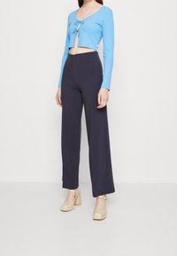 Modrý pruhovaný crop top s dlouhými rukávy a předním zavazováním, kombinovaný s vysokými námořnickými kalhotami se širokými nohavicemi a krémovými platformovými podpatky.