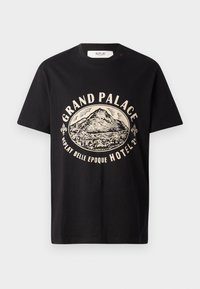T-shirt nera in cotone con stampa grafica beige di una montagna e testo che recita "Grand Palace Replay Belle Epoque Hotel." Design semplice con scollo rotondo.