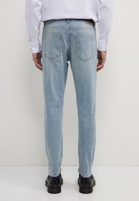 Jeans in denim blu chiaro con una vestibilità dritta, caratterizzati da due tasche posteriori e un minimo di usura. Il tessuto appare liscio con una consistenza morbida.