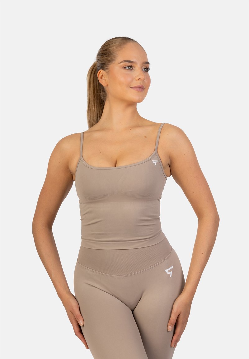 Beige sporttanktop met dunne bandjes, bijpassende high-waisted leggings, beide gemaakt van een gladde, aansluitende stof met een witte logo-accent.