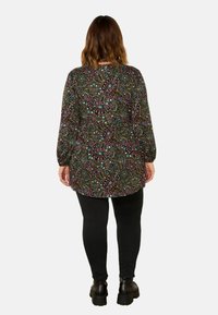 Langarmoberteil in Schwarz mit einem bunten Paisleymuster. Kombiniert mit schwarzen Leggings und stämmigen schwarzen Stiefeln. Weicher Stoff, lockerer Schnitt.