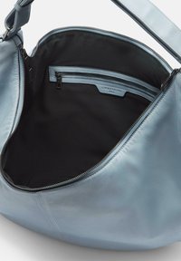 Jasnoniebieska skórzana torebka o gładkiej fakturze, z dużym otwarciem, czarnym materiałowym wnętrzem i kieszonką na suwak. Posiada srebrny zamek.