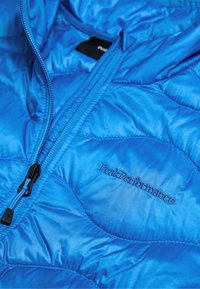 Blå pufferjakke med quiltet tekstur, lynlåslukning og sort "PeakPerformance" logo broderi på brystområdet.