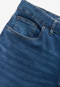 Jeans din denim de culoare albastră închisă, cu un buzunar din spate cu finisaj neted și cusături vizibile, completate cu accente de metal.