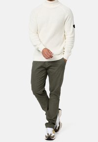 Pull en maille crème avec col montant ; associé à un pantalon vert olive et des baskets blanches avec des accents noirs et camel.