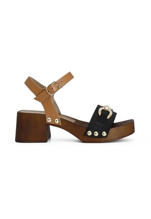 Tan en zwarte sandaal met hak en een chunky blokhak. Voorzien van een enkelbandje met gesp, decoratieve gouden studs en een contrasterend materiaalontwerp.