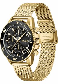Guldtonet rustfrit stål ur med en sort bezel, sort urskive og tre sub-urskiver. Har et vævet mesh-armbånd og datovisning.