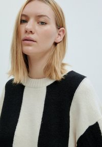 Strickpullover mit vertikalen schwarzen und cremefarbenen Streifen, rundem ribbed Halsausschnitt und weicher Textur. Legere Passform mit überschnittenen Schultern.