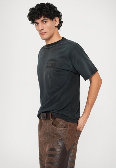 Zwarte katoenen T-shirt met korte mouwen, voorzien van een subtiele logo-print. Gecombineerd met bruine textuurbroek en een donkere riem.