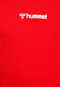 Rotes Sportshirt mit strukturierter Oberfläche, V-Ausschnitt und einem weißen "hummel"-Logo auf der Brust.