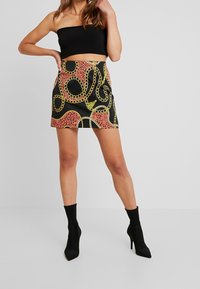 Crop top noir, ajusté. La mini jupe présente un fond noir avec un imprimé animal rose et un motif de chaîne jaune. Le mannequin porte des bottines noires.
