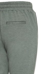 Sive jogging hlače od mekanog materijala, s teksturiranom površinom, elastičnim pojasom i detaljem stražnjeg džepa.