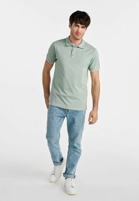 Jasnozielona koszulka polo z krótkim rękawem, zapięta na guziki, z niebieskimi akcentami. Połączona z jasnoniebieskimi dżinsami i białymi trampkami.