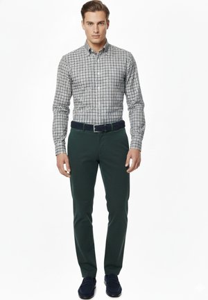 Camisa de cuadros en blanco y negro, combinada con pantalones verde oscuro, complementada con un cinturón azul marino y zapatos oscuros.