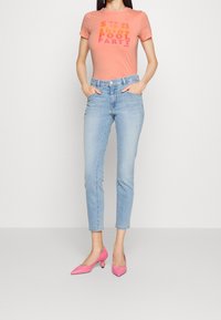 Ljust rosa t-shirt med flerfärgad grafiktext, i kombination med ljus tvättade, åtsittande jeans och rosa högklackade skor med rundad tå.