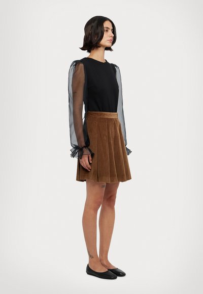 Haut noir avec des manches transparentes et bouffantes ; jupe plissée en velours côtelé marron ; ballerines noires. Texture lisse et silhouette ajustée.
