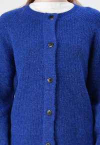 Blue knit cardigan made from soft, textured material, featuring a round neck and six black buttons down the front.