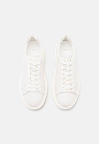 Baskets en cuir blanc avec bout arrondi, lacets plats blancs et logo subtil sur le côté. Texture lisse et design épuré.