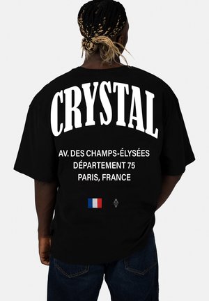 Zwart oversized t-shirt met grote witte tekst "CRYSTAL" en aanvullende tekst met locatiegegevens. Inclusief afbeelding van de Franse vlag.