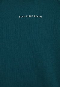 Teal crewneck sweatshirt iz mehkega bombaža, s kratkim belim napisom "BLUE RIDGE DENIM" natisnjenim spredaj, z gladko teksturo.