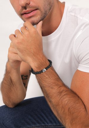 Schwarzes Lava-Perlenarmband mit einem silbernen Akzent. Der Stil umfasst sphärische Perlen, eine strukturierte Oberfläche und ein einfaches, elastisches Design.