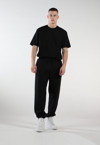 Schwarzes Kurzarm-T-Shirt und schwarze Sweathosen mit Kordelzug, kombiniert mit weißen High-Top-Sneakers. Glatter Stoff, lockere Passform, keine Muster.
