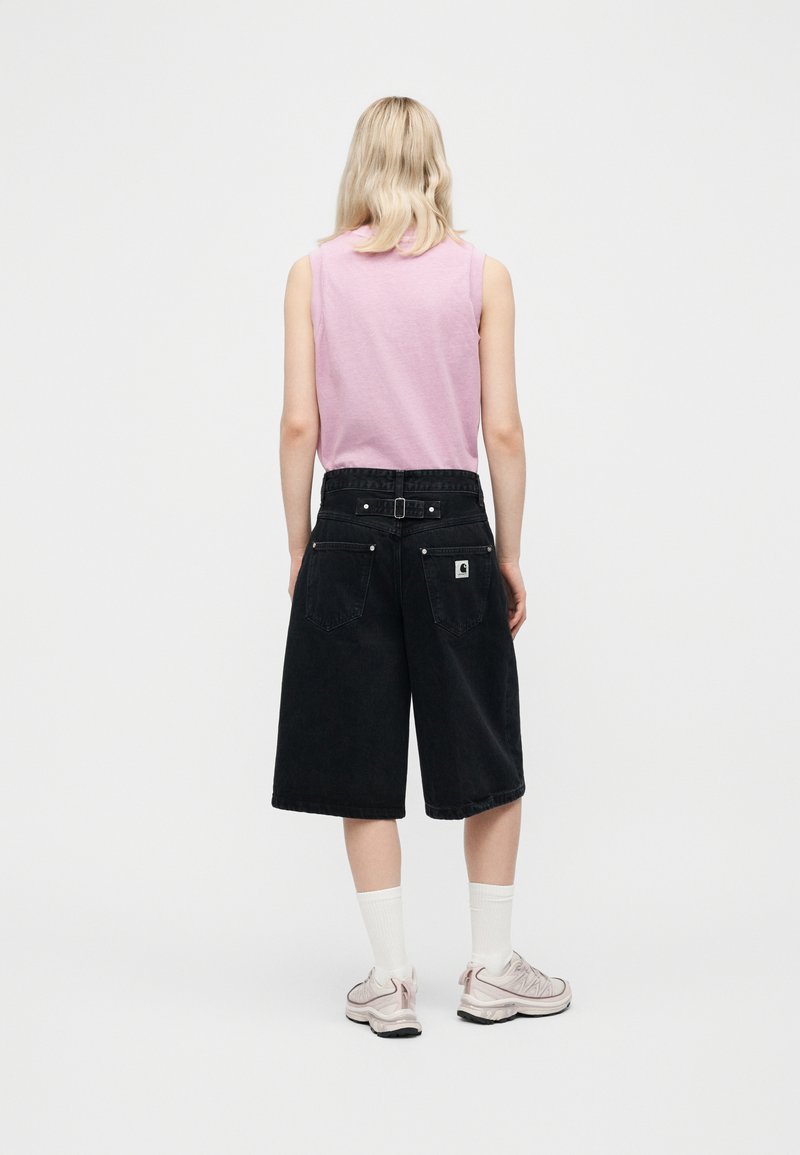 Blonde person wearing sleeveless pink top, black wide knee-length shorts with back pockets, white socks, and light pink sneakers, standing facing away.