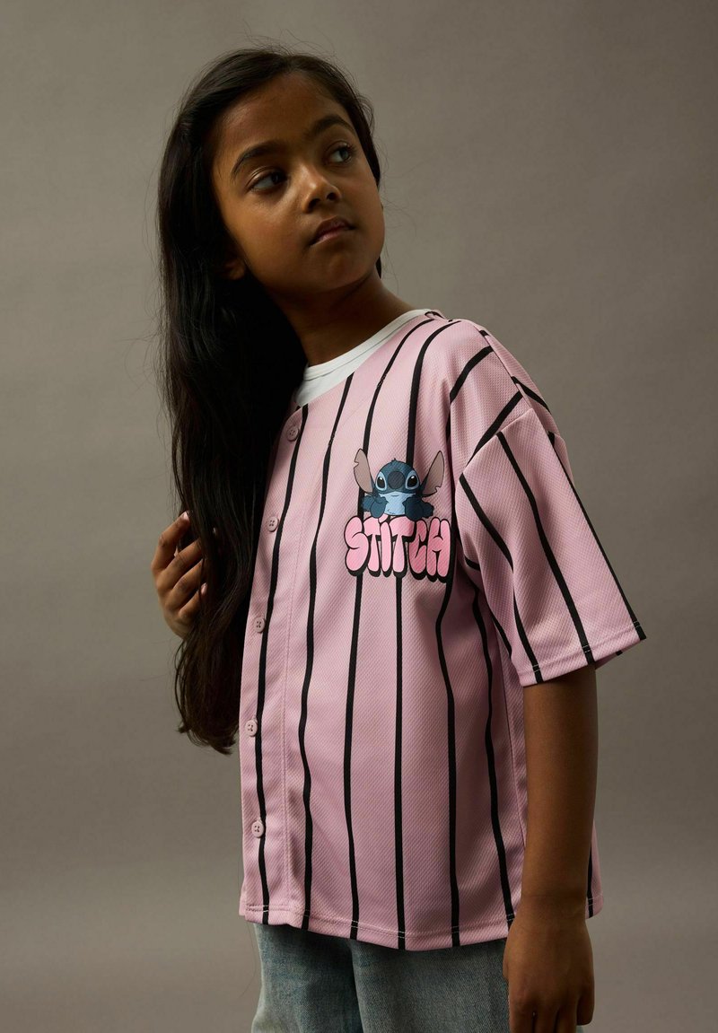 Roosa pesapallijersey mustade triipudega, millel on Stitchi graafika ja tekst "STITCH" julge roosa tähekirjaga. Valmistatud hingavast tekstuuriga kangast.