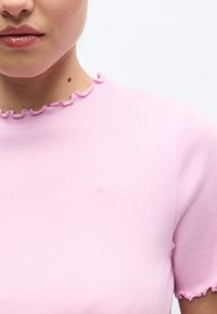 Ροζ ριμπ μπλουζάκι με κυματιστό ντεκολτέ και κοντά μανίκια. Διαθέτει διακριτικό κεντημένο λογότυπο στο στήθος με ίδιο χρώμα κλωστής.