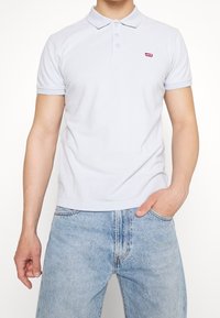 Světle modré polo tričko vyrobené z bavlny, s klasickým límečkem a třemi knoflíky, se malým červeným logem Levi's na hrudi.