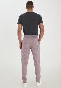 Graues Baumwoll-T-Shirt kombiniert mit hellmaronfarbenen Jogginghosen. Die Hose hat eine strukturierte, melierte Optik und einen elastischen Bund und wird mit weißen Turnschuhen getragen.