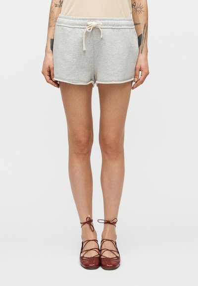 Shorts en coton gris avec taille à cordon, dotés d'une texture douce et de coutures contrastantes de couleur claire. Portés avec des chaussures en cuir marron.