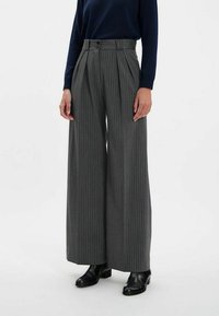 Pantalons larges à rayures grises avec taille haute, dotés de double boutons et de plis, associés à des bottines noires.