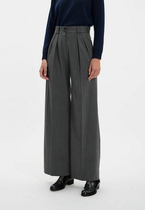Pantalons larges à rayures grises avec taille haute, dotés de double boutons et de plis, associés à des bottines noires.