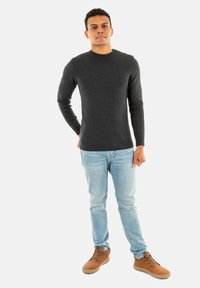 Maglione grigio a maglia con colletto a costine, abbinato a jeans azzurri chiari e scarpe beige. Il maglione presenta piccoli bottoni sulla spalla.