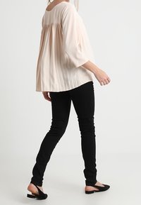 Blusa plissettata rosa chiaro con maniche 3/4, abbinata a jeans neri slim e scarpe basse nere, vista da dietro.