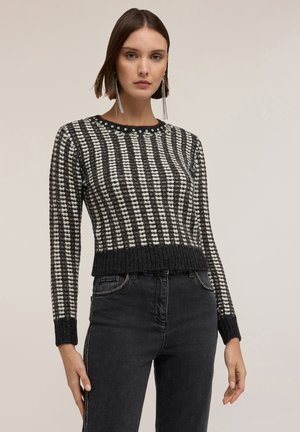 Suéter de punto en blanco y negro con un patrón de rayas, cuello redondo y dobladillo acanalado. Combinado con jeans oscuros, mostrando un diseño ajustado.