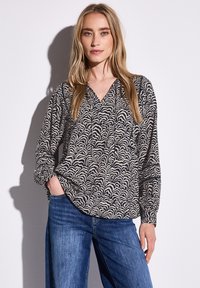 Långärmad blus i svart och krämfärgad vågmönster, med V-ringning och avslappnad passform. Matchad med ljusblå denimjeans.