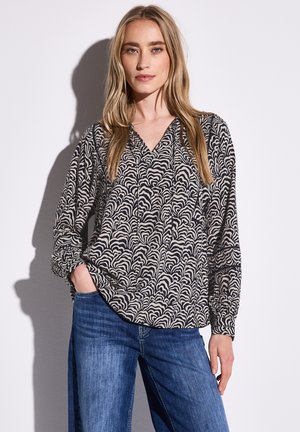 Långärmad blus i svart och krämfärgad vågmönster, med V-ringning och avslappnad passform. Matchad med ljusblå denimjeans.